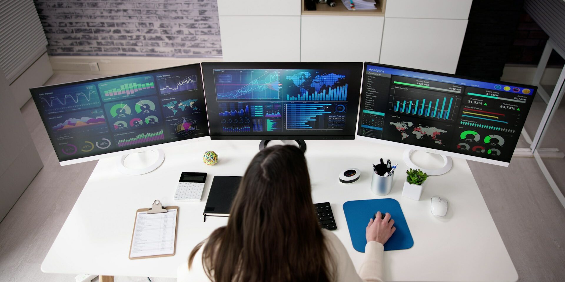 woman data scientist sitting at a computer with three screens of data