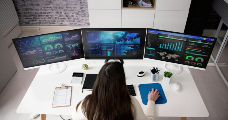 woman data scientist sitting at a computer with three screens of data