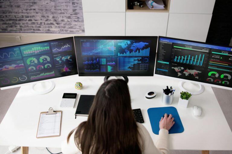 woman data scientist sitting at a computer with three screens of data