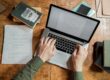 birdseye view of a laptop, book, and sheet of paper. with hands typing on keyboard How to hire a copywriter