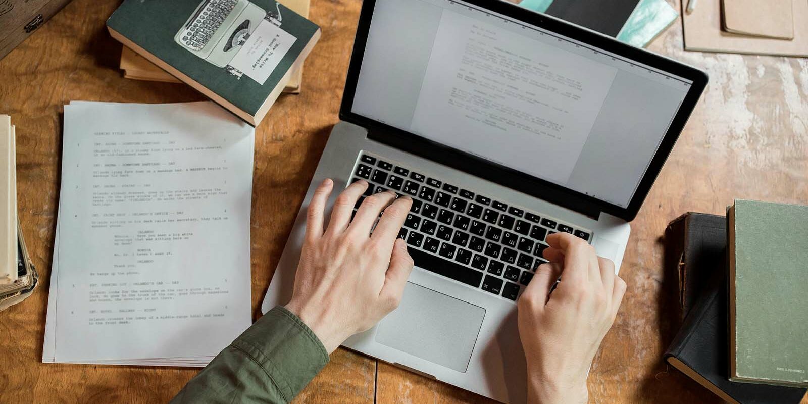 birdseye view of a laptop, book, and sheet of paper. with hands typing on keyboard How to hire a copywriter