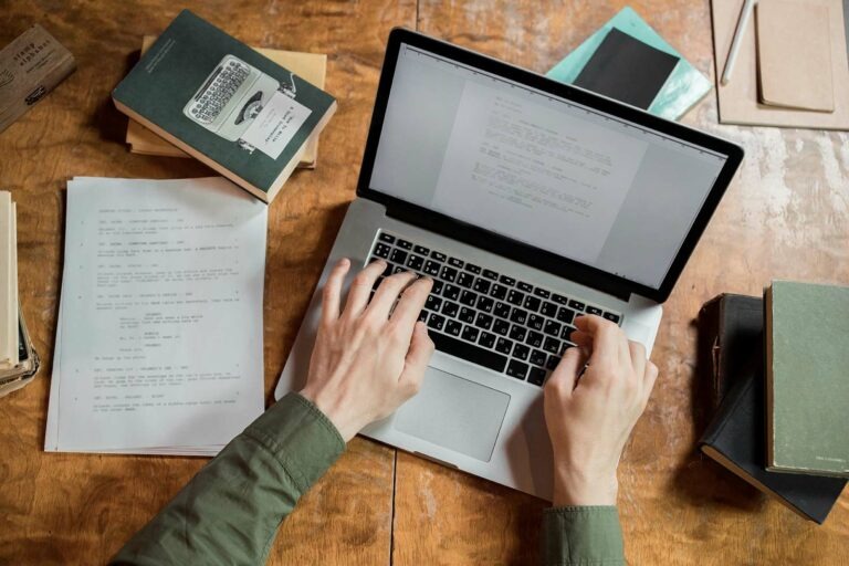 birdseye view of a laptop, book, and sheet of paper. with hands typing on keyboard How to hire a copywriter